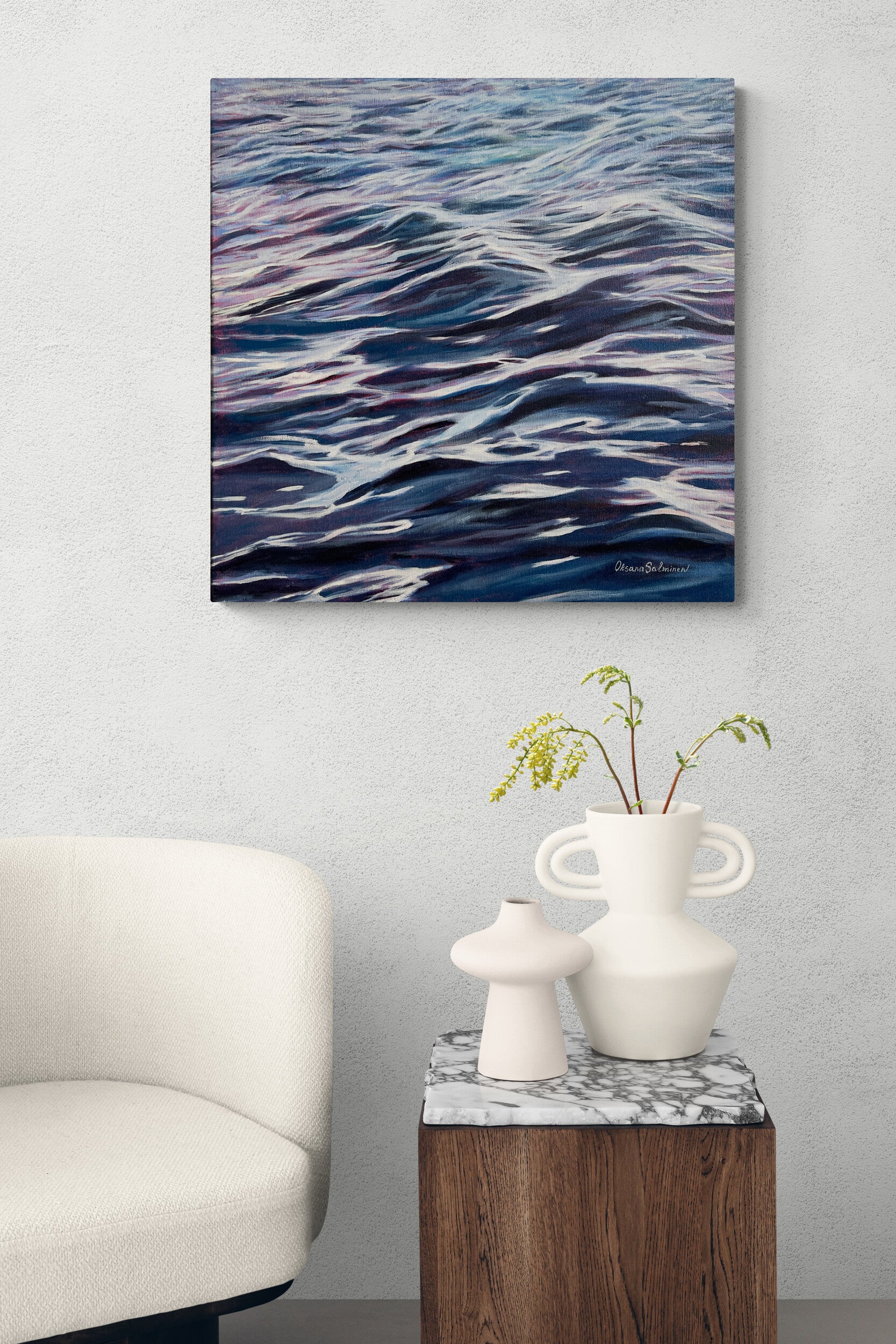 Abstract painting of wavy blue and white patterns on a wall above a white chair and small table with decorative items.