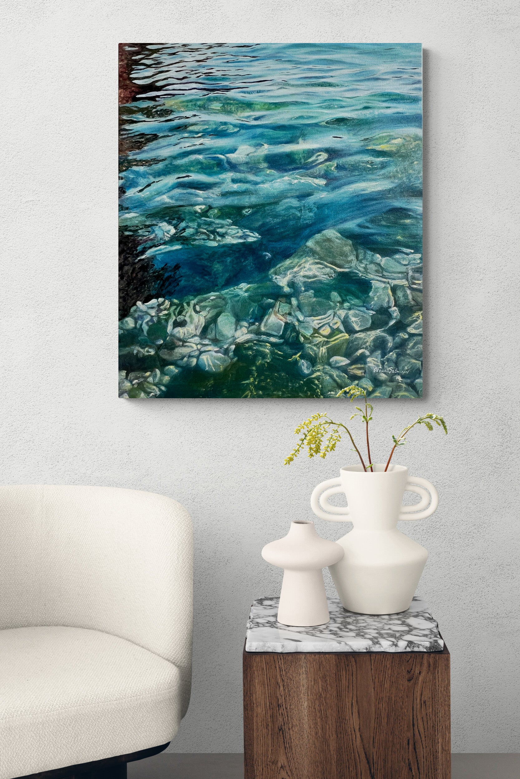 Canvas print of water with stones on a wall above a white armchair and side table with decorative items.