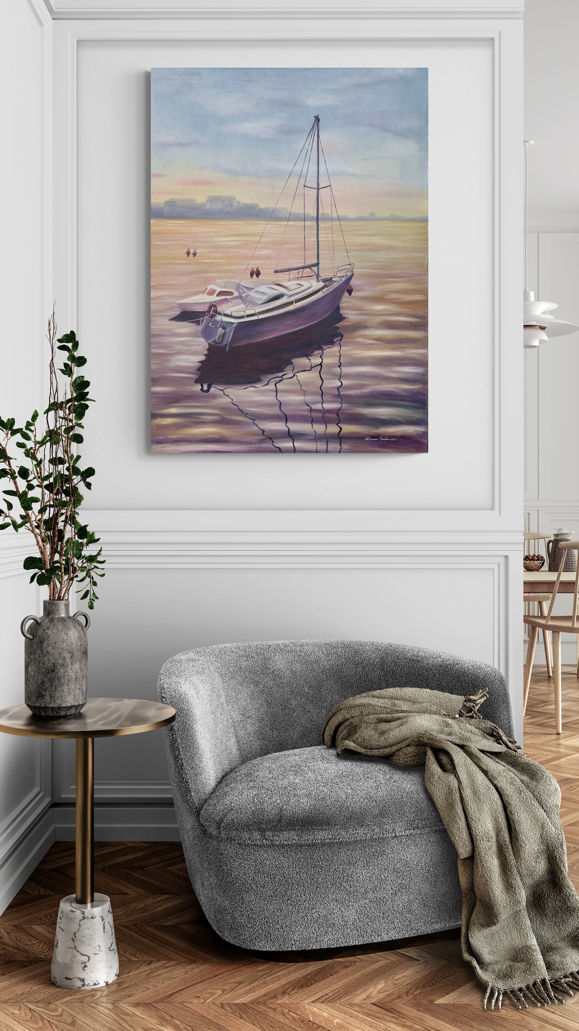 Gray armchair with a blanket next to a side table, with a painting of a boat on the wall above.