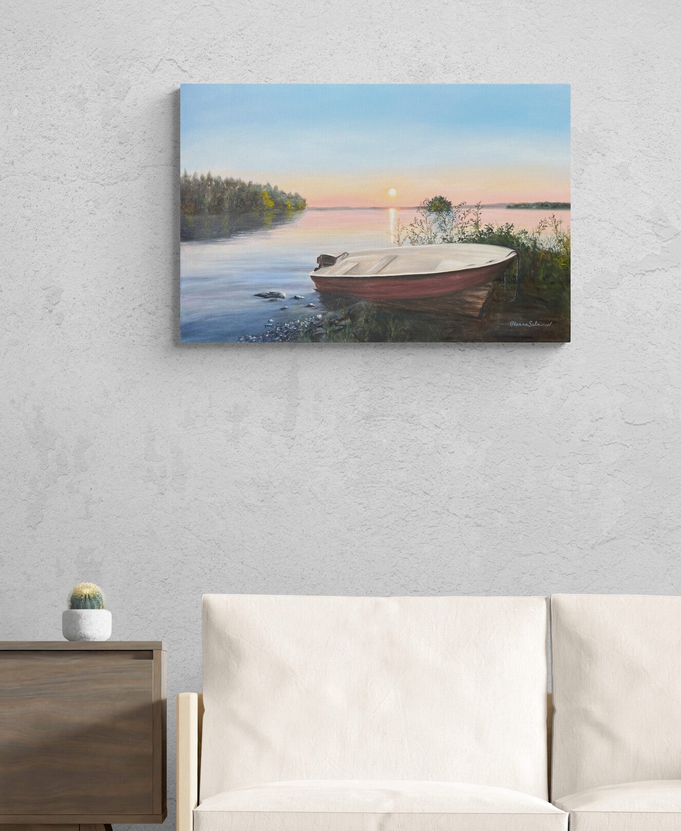 Painting of a boat on a lake with a sunset, hanging on a wall above a sofa.