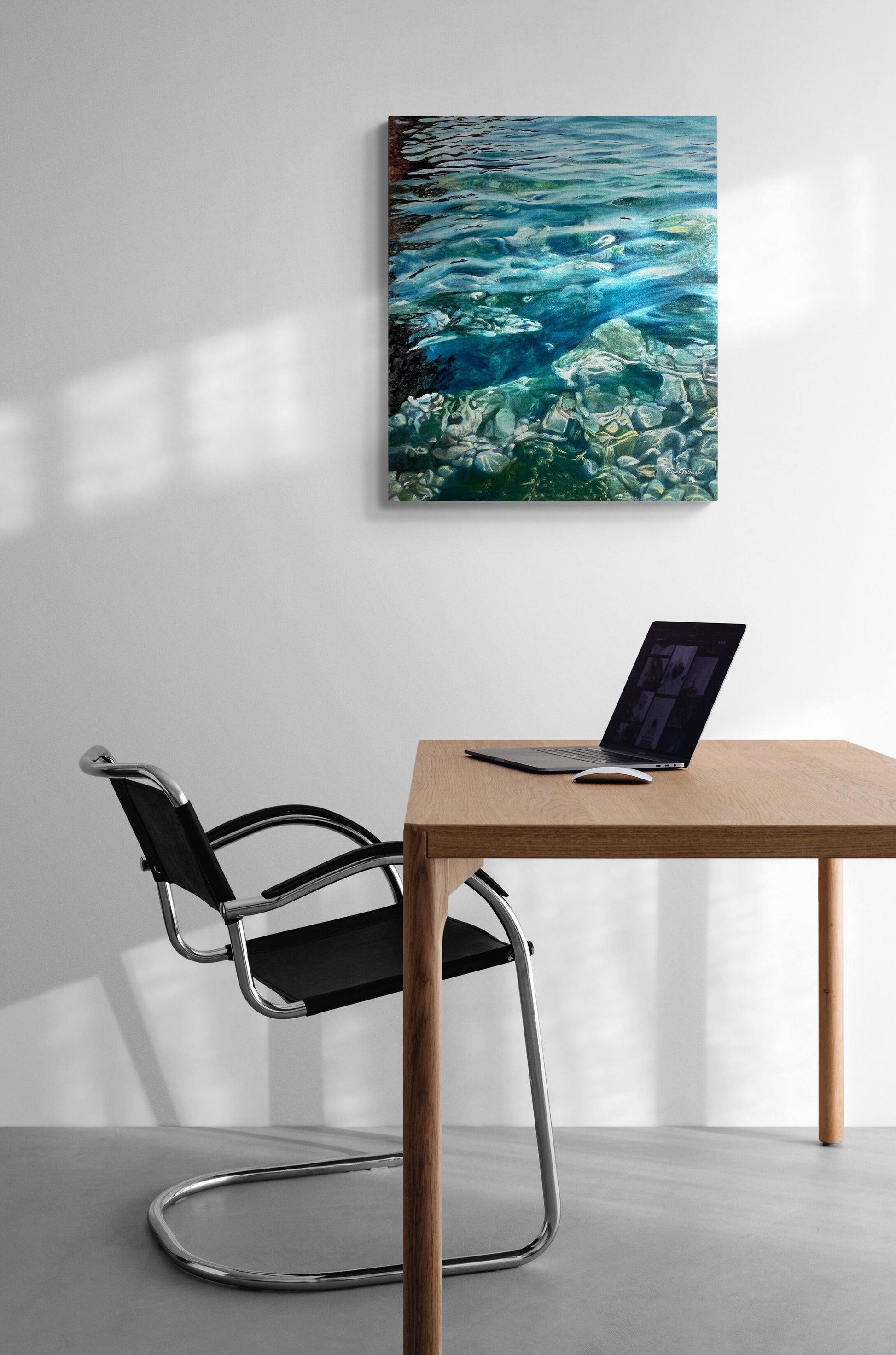 Modern office setup with a desk, chair, and laptop next to a large wall art of water.