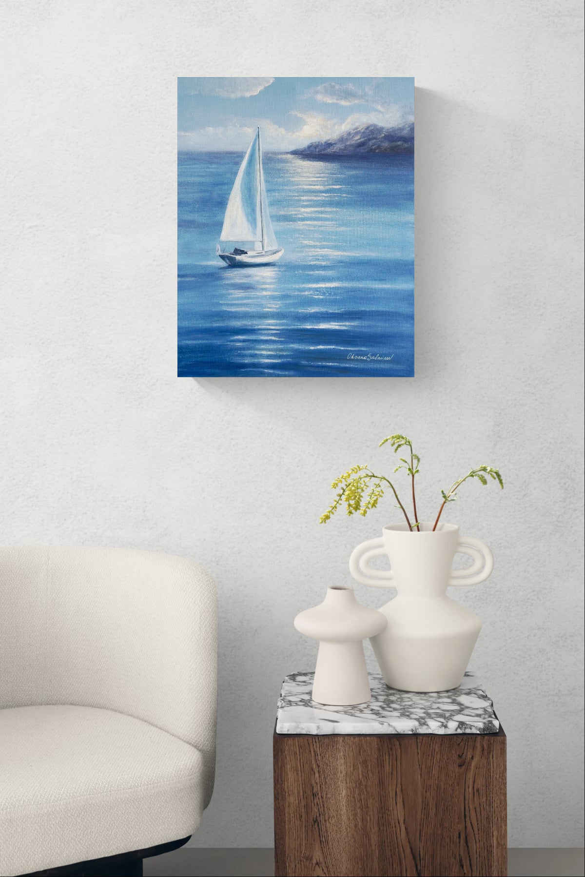 A vertical canvas print of a sailboat painting on a blue sea, styled in a modern living room setting above a side table with vases and a chair.
