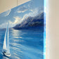 A canvas painting of a sailboat on a blue sea with mountains and clouds, shown hanging against a light wall.