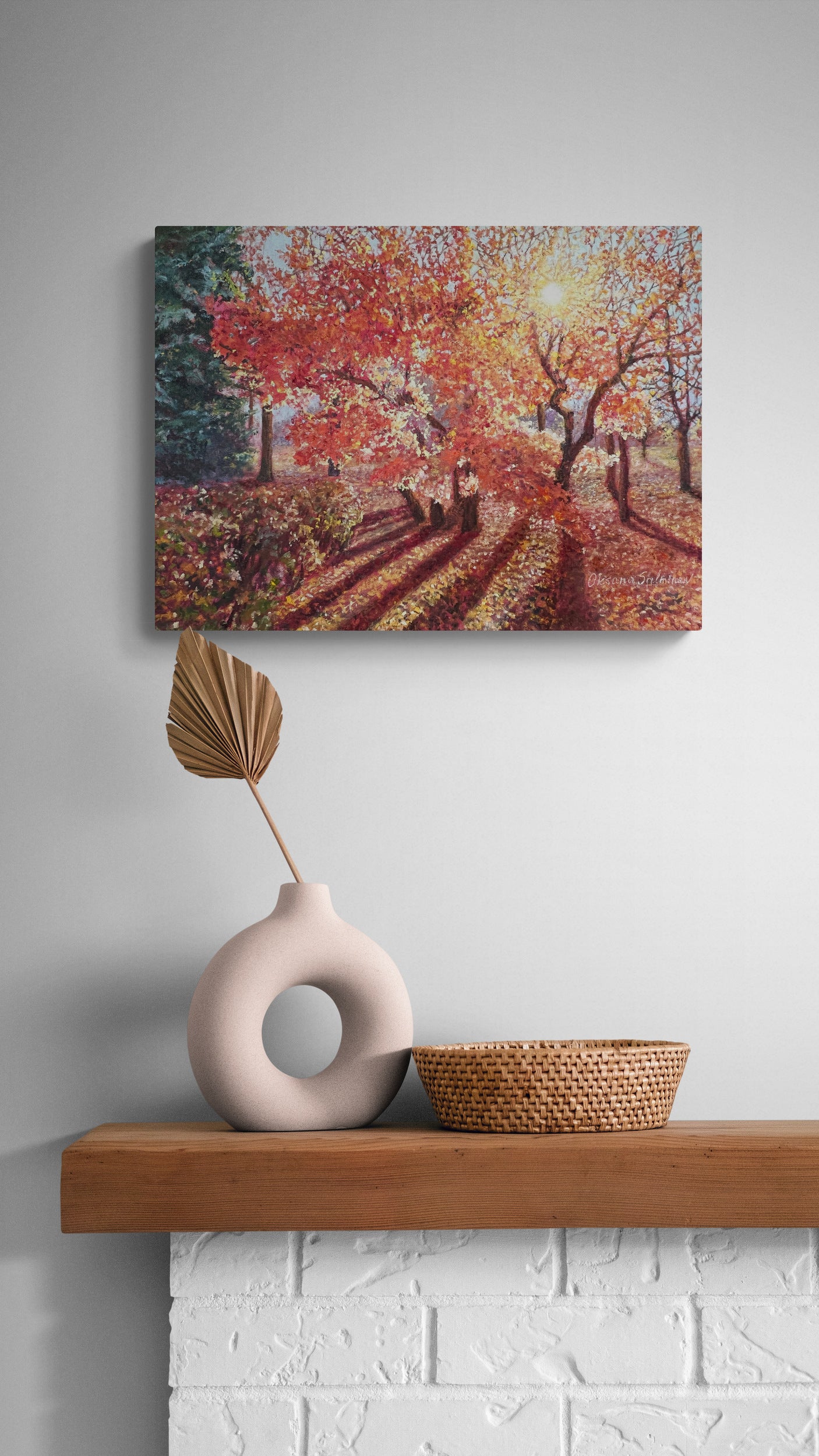 Oil painting of an autumn scene on a wall above a wooden shelf with decorative items.