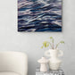 Abstract painting of wavy blue and white patterns on a wall above a white chair and small table with decorative items.