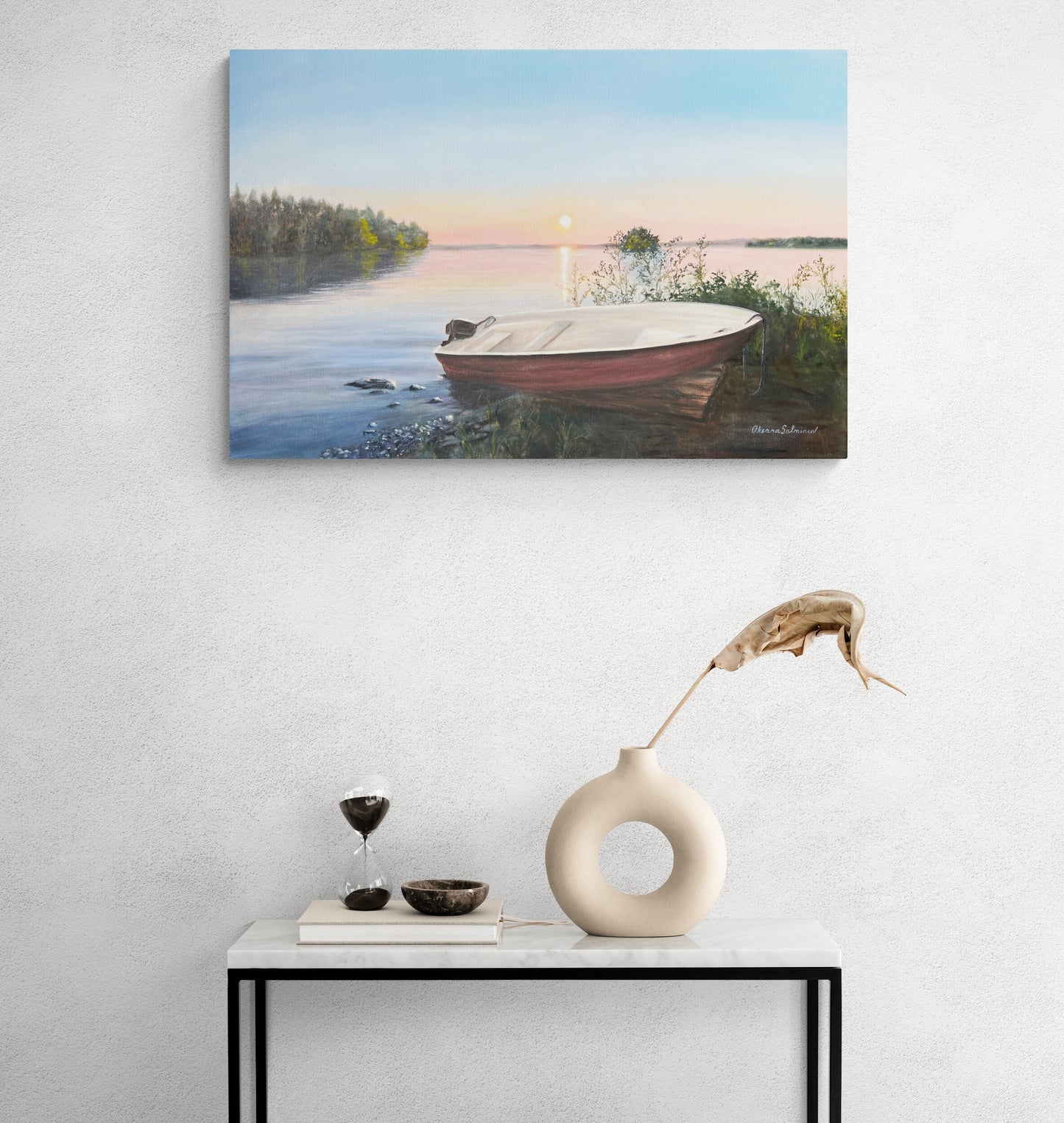 Painting of a boat on a lake with a sunset, displayed on a wall above a table with decorative items.