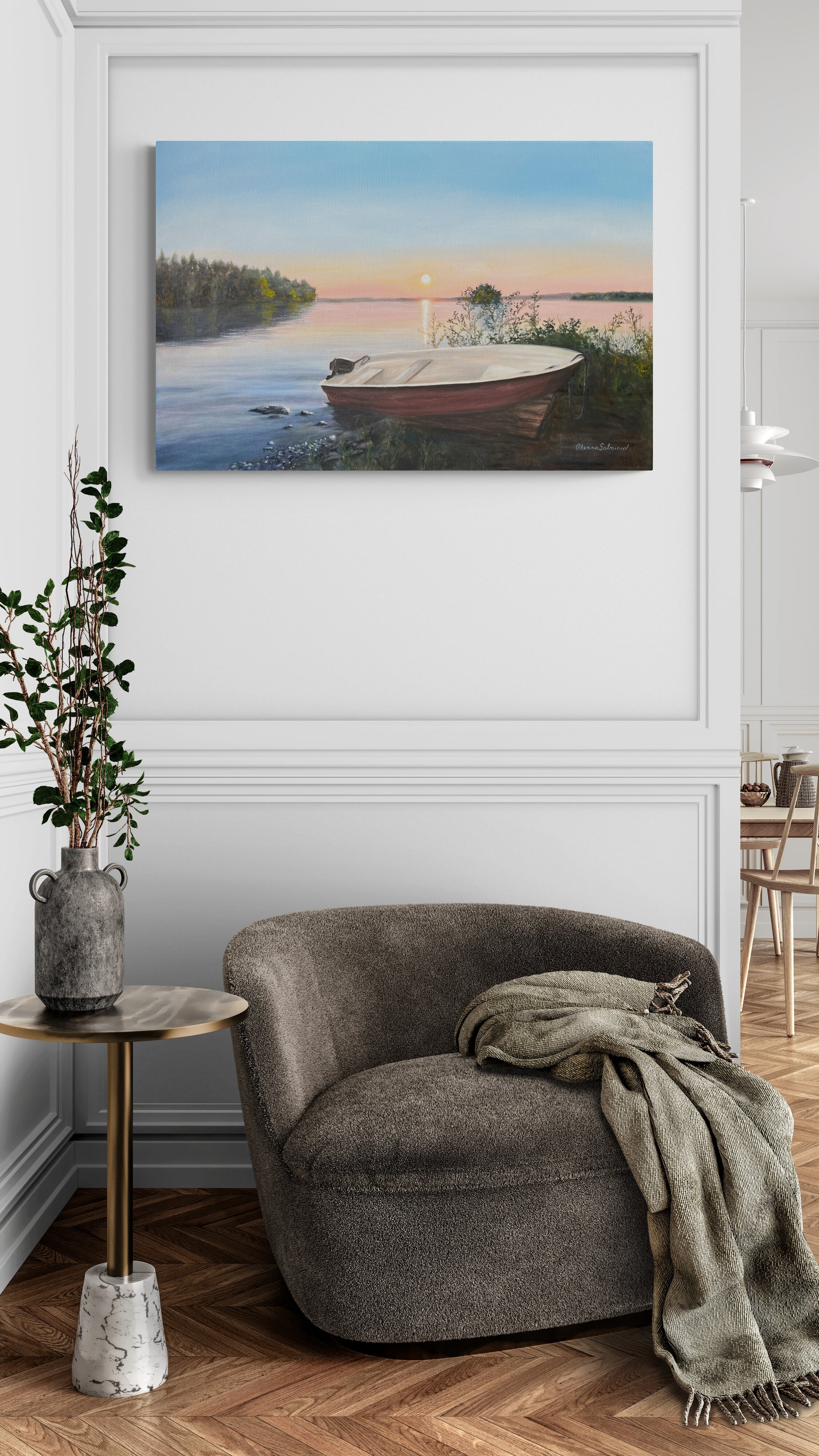 Unframed painting of a boat on a lake above a gray armchair with a blanket in a room.
