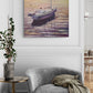 Gray armchair with a blanket next to a side table, with a painting of a boat on the wall above.