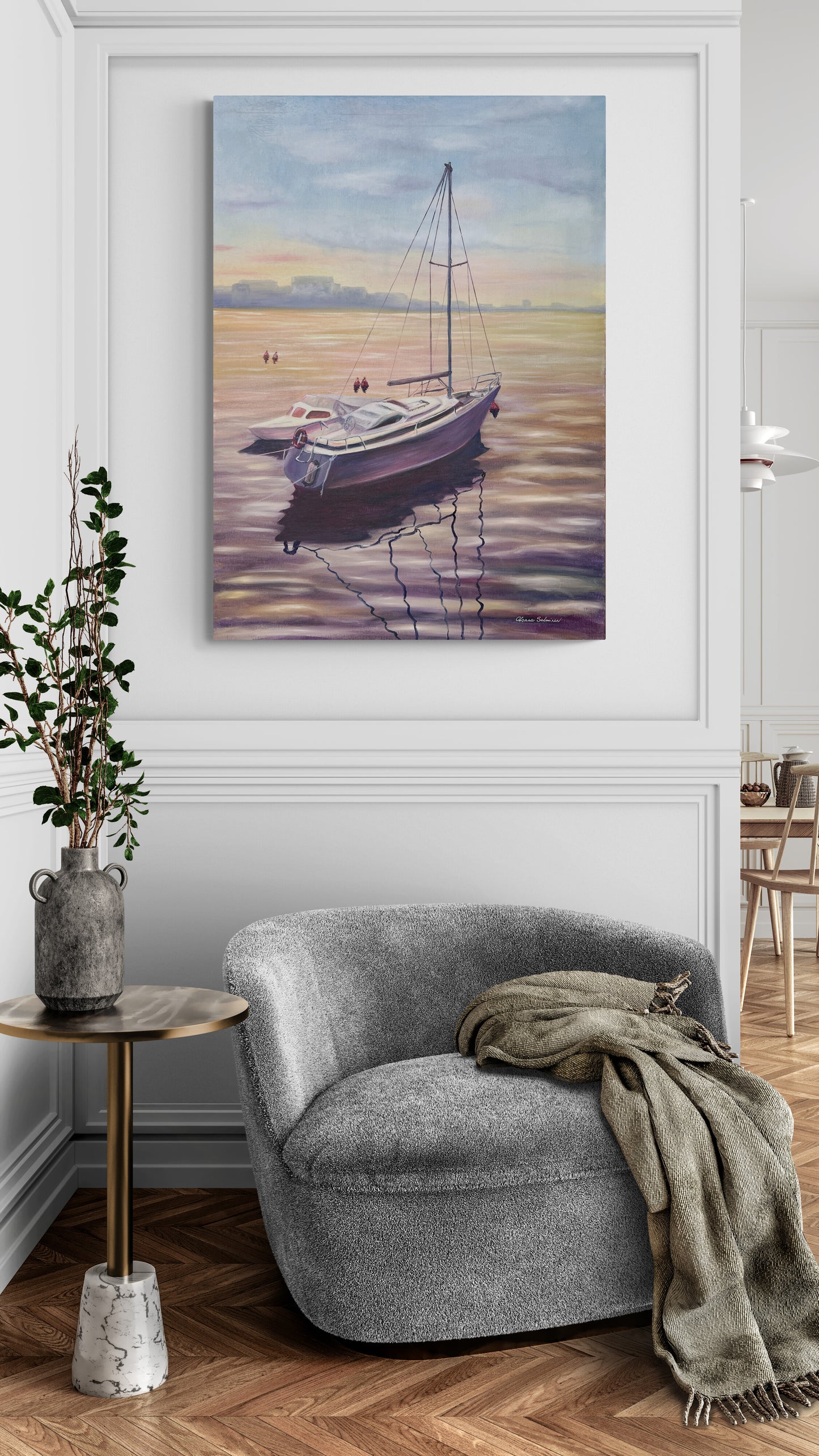 Gray armchair with a blanket next to a side table, with a painting of a boat on the wall above.