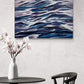 Abstract painting of wavy blue and purple patterns on a wall above a table with a vase and chair